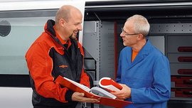 Zwei Männer im Gespräch über Werkzeuge im Lieferwagen Ein Vissmann Mitarbeiter zeigt einem Kunden, einen Ordner vor einem Firmenbulli