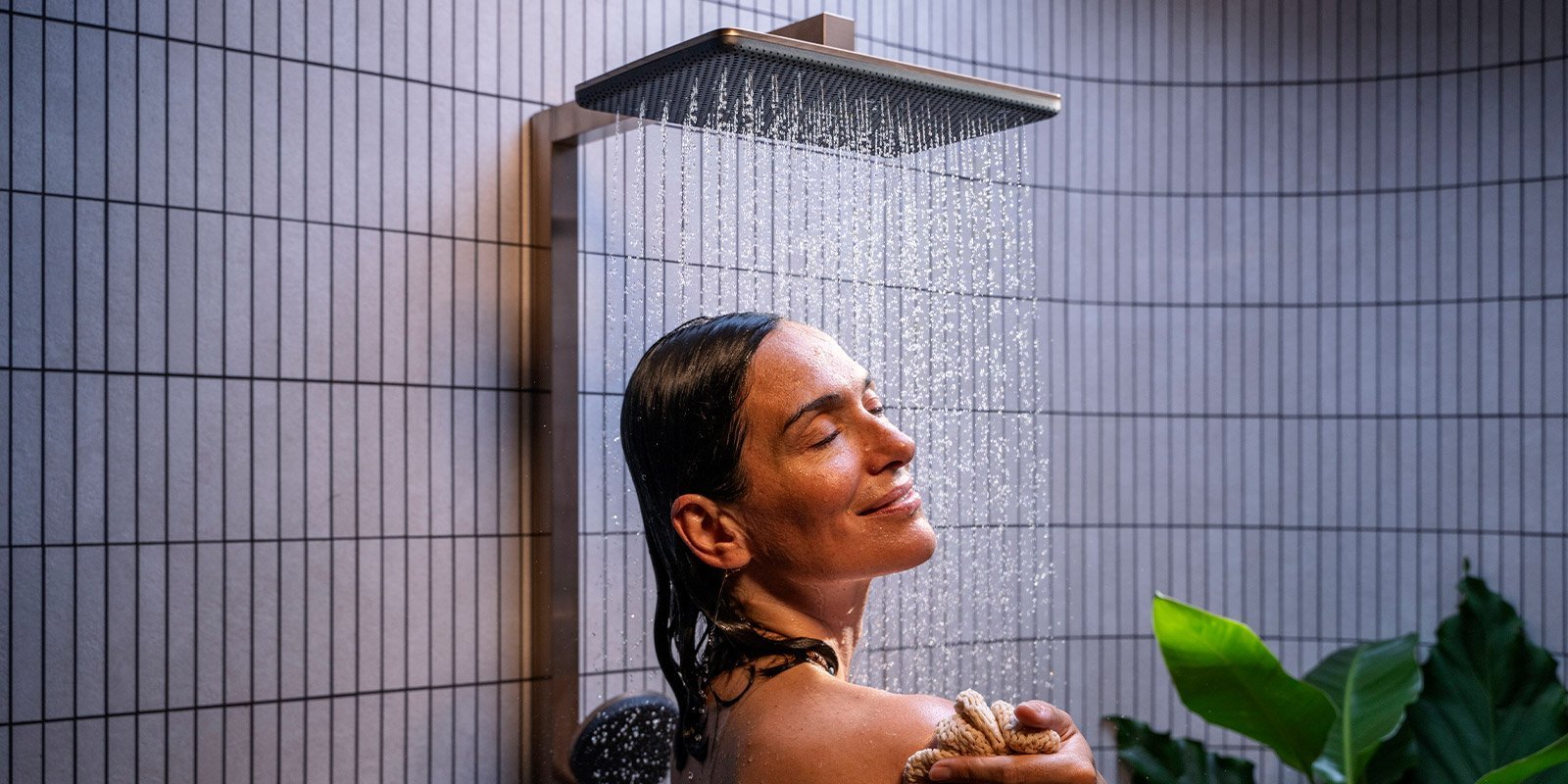 Entspannende Dusche mit sanftem Wasserfluss und Pflanzen Eine Frau genießt eine erfrischende Dusche, während Wasser sanft über ihr Gesicht fließt und sie entspannt lächelt.