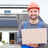 Ein Mann in Arbeitskleidung vor einer Photovoltaikanlage mit einem Laptop in der Hand