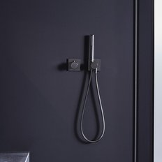 Eine moderne Dusche mit einem eleganten schwarzen Wandsystem und einem flexiblen Duschkopf, der an der Wand hängt.