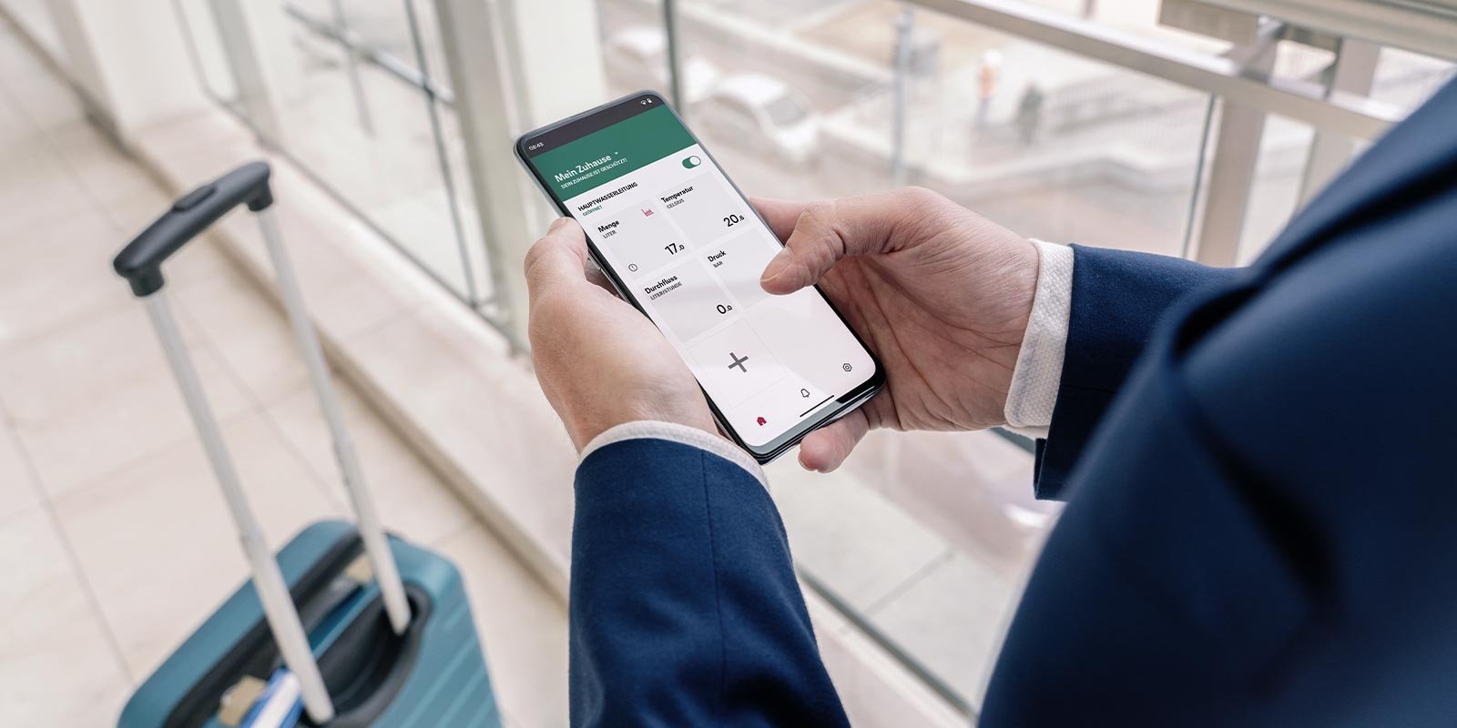 Moderne Technologie: Smartphone-Nutzung am Flughafen Eine Person in einem Anzug hält ein Smartphone und überprüft die Temperatur und Luftfeuchtigkeit in einem modernen Raum.